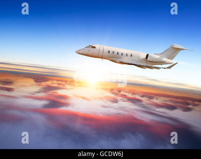 Privaten Düsenjet fliegt über Wolken bei Sonnenuntergang. Schuss aus Frontansicht Stockfoto