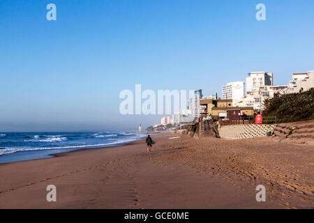 Männliche Surfer am Strand am frühen Morgen gegen gewerbliche und private Anlagen in Umhlanga Rocks Stockfoto