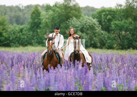 Die Braut und Bräutigam Reiten auf dem Pferd über ein Feld von lupine Stockfoto