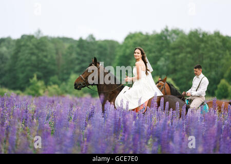 Die Braut und Bräutigam Reiten auf dem Pferd über ein Feld von lupine Stockfoto