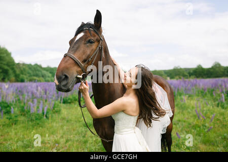 Die Braut stand mit Pferd auf einem Feld von lupine Stockfoto