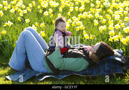 Die dreimonatige Cecily Dargan genießt ihr erstes Osterfest mit ihrer Mutter Helen, die mit ihr am Osterfeiertag in Worthing, West Sussex, zwischen den Narzissen am Meer sitzt. Stockfoto