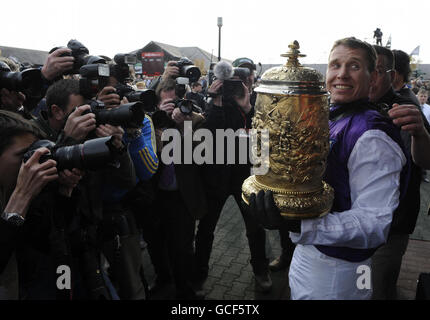 Der Jockey Richard Johnson posiert mit der Trophäe vor einer großen Menge von Fotografen nach dem Sieg auf Planet of Sound beim Guinness Gold Cup in Punchestown während des Punchestown Festivals auf der Pferderennbahn in Punchestown, Dublin, Irland. Stockfoto