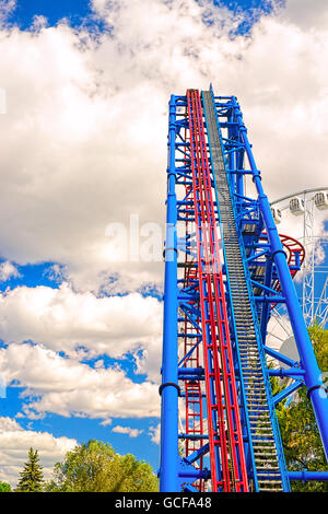 Blick auf den langen Aufstieg auf einer Achterbahn in einem wolkigen Himmel gerichtet. Warme farbige Landschaft im Vergnügungspark am sonnigen Tag Stockfoto