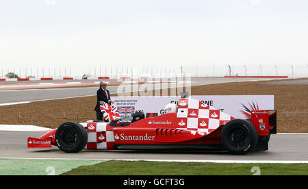 Sir Jackie Stewart winkt die Unionsflagge, um den Duke of York und den BRDC-Präsidenten Damon Hill in einem zweisitzigen Rennwagen des neuen Silverstone Circuit auf eine Eröffnungsrunde zu schicken. Stockfoto