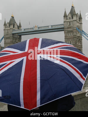 Ein Mann versteckt sich unter einem Regenschirm mit Gewerkschaftsjackern bei der Tower Bridge in London. Stockfoto