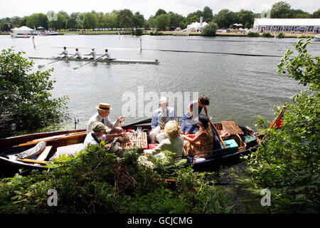 Am ersten Tag der alljährlichen Henley Royal Regatta in Henley-on-Thames, Oxford, essen die Leute in einem Boot zu Mittag, während eine Crew zur Startlinie geht. Stockfoto