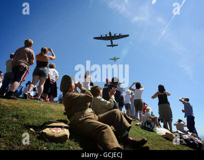 Die Zuschauer winken, während ein Lancaster Bomber und ein Spitfire das National Memorial in Capel-le-Ferne, Kent, im Rahmen einer Veranstaltung anlässlich des 70. Jahrestages der Schlacht von Großbritannien überwölben. Stockfoto