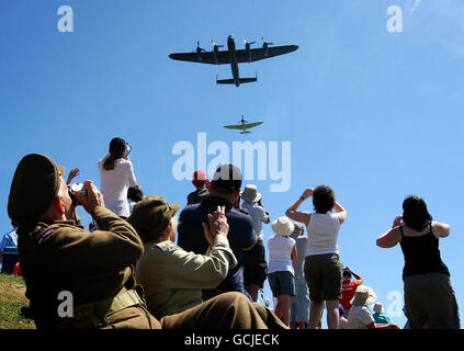 Die Zuschauer winken, während ein Lancaster Bomber und ein Spitfire das National Memorial in Capel-le-Ferne, Kent, im Rahmen einer Veranstaltung anlässlich des 70. Jahrestages der Schlacht von Großbritannien überwölben. Stockfoto