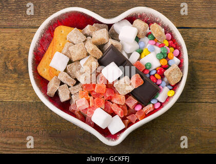 Andere Art von Zucker, Süßigkeiten und Gebäck im Herzen geformte Schale. Ungesunde Ernährungskonzept. Ansicht von oben Stockfoto