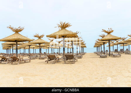 Strand mit strohgedeckten Sonnenschirmen und Liegestühlen aus Holz. Stockfoto