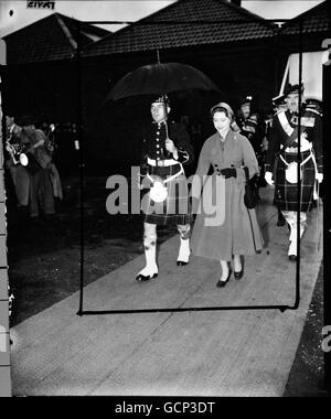 Ein Highlander trägt und einen Regenschirm, um Prinzessin Margaret vor dem Regen zu schützen, während sie zu ihrem Auto geht, nachdem sie dem 1. Bataillon The Highland Light Infantry, dessen Regiment sie am 19. Oktober 1955 Oberst im Bulford Camp in Wiltshire ist, neue Farben vorgestellt hat. Wegen des Regens führte die Prinzessin die Zeremonie in einem großen Schuppen im Lager durch. Stockfoto