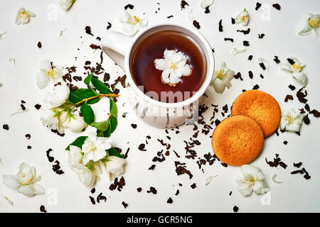 Teetasse mit getrockneten Blättern und duftenden Jasminblüten und Cookie auf weißem Hintergrund. Ansicht von oben Stockfoto