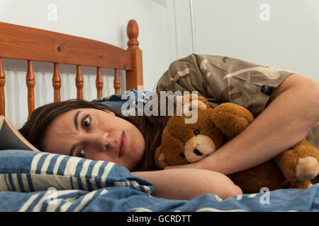 Eine aufgeregt junge Frau umarmt einen Teddybär im Bett Stockfoto