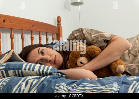 Eine aufgeregt junge Frau umarmt einen Teddybär im Bett Stockfoto