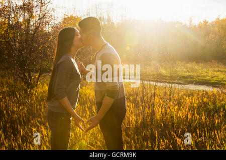 Eine junge asiatische paar küssen in einem Park im Herbst und ein Herz mit ihren Händen in die Wärme der untergehenden Sonne; Edmonton, Alberta, Kanada Stockfoto