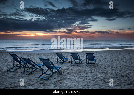 Sechs Liegestühle am Strand mit Sonne und Wellen Stockfoto