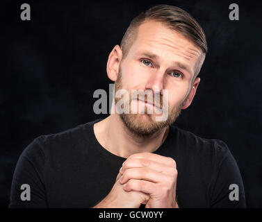 Junger Mann bittet um Vergebung auf einem dunklen Hintergrund. Stockfoto