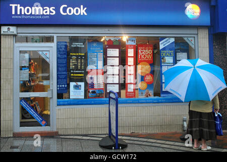 Eine ältere Frau schützt sich vor dem Regen unter einem Regenschirm, während sie im Fenster von Thomas Cook auf die Feiertage schaut Stockfoto