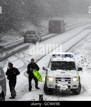 Polizeibeamte leiten einen Gitterwagen, da eine Straße über den North Yorkshire Moors heute nach Schneefällen und Schneestürmen gesperrt wurde. Stockfoto