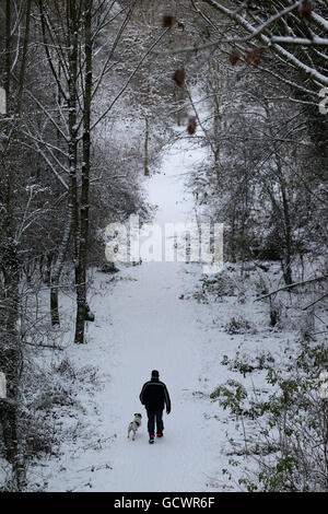 Ein Mann geht mit einem Hund auf einer schneebedeckten Gasse in Bingham, Nottinghamshire, während in Großbritannien weiterhin Schnee fällt. Stockfoto