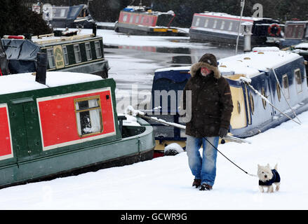 Ein Mann geht mit einem Hund auf dem schneebedeckten Schlepptweg in Mercia Marina in Derbyshire, während in Großbritannien weiterhin Schnee fällt. Stockfoto