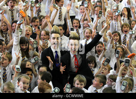 John (blaue Krawatte) und Edward Grimes aka Jedward mit Schülern von Craigdhu Primary, die vor ihrem Konzert in Glasgow eine Recycling-Kampagne zugunsten von Childline in Milngavie auf ihrer Schulversammlung fördern. Stockfoto