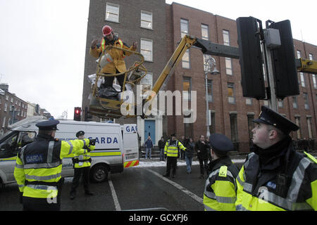 Ein Mann benutzt einen mit einer Reihe von Slogans überzogenen Kirschpflücker, um vor den Toren des Leinster House, Dublin, zu protestieren und unterhält sich am Budgettag mit gardai. Stockfoto