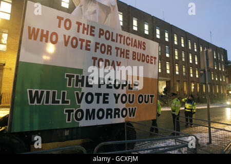 Gardai steht neben einem Cherry Picker, der mit einer Reihe von Slogans bedeckt ist, die Politiker und den Bankensektor angreifen, um am Budgettag vor den Toren des Leinster House, Dublin, zu protestieren. Stockfoto