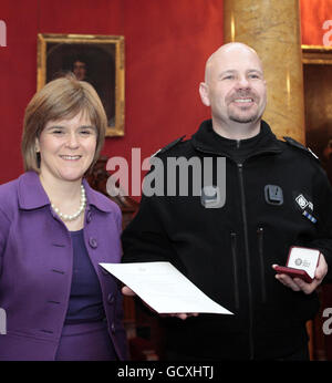 Die stellvertretende erste Ministerin Nicola Sturgeon mit dem Constable Stewart Ferguson - einer von sieben Männern, die vor drei Jahren den versuchten Terroranschlag auf den Flughafen Glasgow vereitelte und heute für ihre Tapferkeit anerkannt wurden, als sie in der Royal Collage of Physicians in Edinburgh die Auszeichnung der Königin für Tapferkeit erhielten. Stockfoto