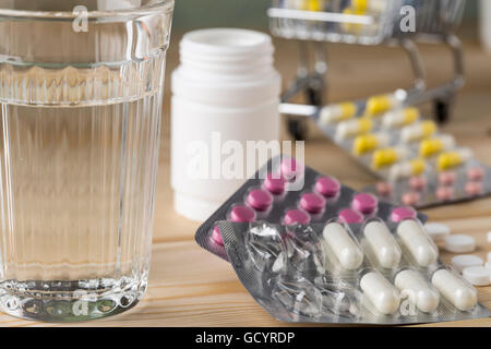 Glas von sauberem Wasser und ein paar Packungen bunte Pillen und Kapseln Stockfoto