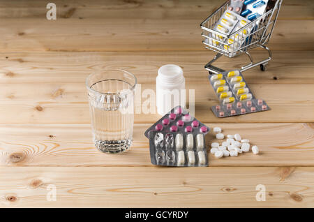 Glas sauberes Wasser und Haufen Blister-Packungen von Pillen mit Shop trolley Stockfoto