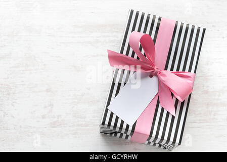 Geschenkbox verpackt in schwarz / weiß gestreiftes Papier mit rosa Schleife auf weißem Holz alte Hintergrund. Leere Notiz über gebunden. Stockfoto