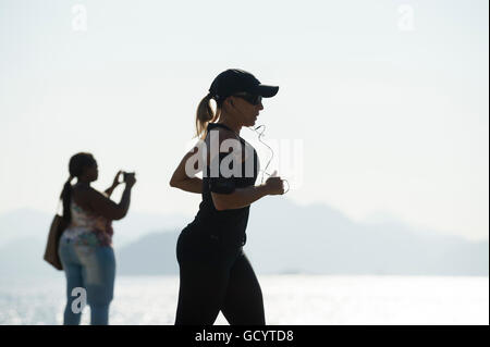 RIO DE JANEIRO - 3. April 2016: Ein Jogger übergibt Silhouette vor einem hellen Morgen Blick vom Copacabana Strand entfernt. Stockfoto