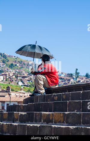 Mann mit Regenschirm unter einem strahlend blauen Himmel in Cusco, Peru Stockfoto