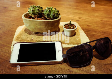 Wohnung lag auf hölzernen Hintergrund mit textfreiraum Shot Handy, Brille und Kakteen. Stockfoto