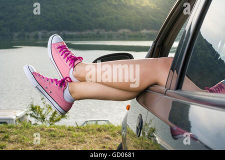 Frau Beine aus dem Autofenster am See Stockfoto