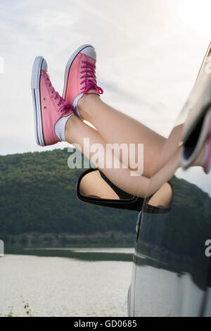 Frau Beine aus dem Autofenster am See Stockfoto