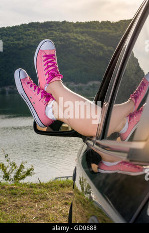 Frau Beine aus dem Autofenster am See Stockfoto