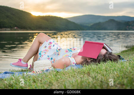 Junge Frau schläft mit einem Buch am See. Solo-Entspannung Stockfoto