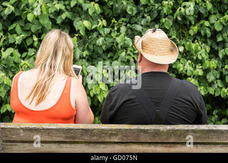 Eine Frau, die auf einem iPhone schreibt, während sie auf einer Parkbank neben ihrem männlichen Partner sitzt Stockfoto