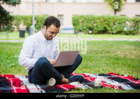 Man arbeitet mit Laptop im Park. Outdoor, Kerl aussehen herausgefordert und denken Stockfoto