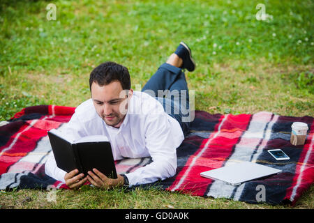 hübscher junger Geschäftsmann Buch liegen im park Stockfoto