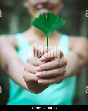 Lächelnde Frau Ginkgo Biloba Blatt in ihren Händen hält Stockfoto