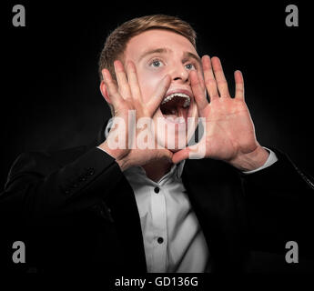 Kaufmann im schwarzen Anzug, ruft seine Hände anheben. auf einem dunklen Hintergrund. Stockfoto