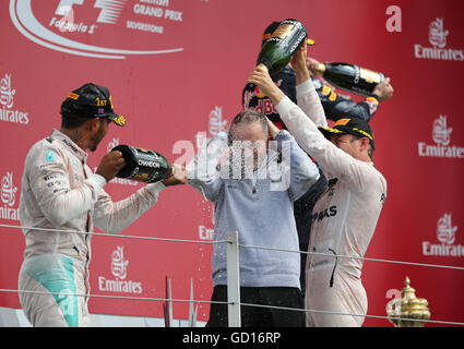 Mercedes Lewis Hamilton (links) und Ferrari Sebastian Vettel spray Team principal Paddy Lowe (Mitte) während des 2016 British Grand Prix in Silverstone, Towcester. Stockfoto