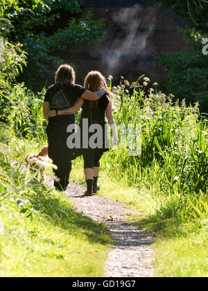 Junges Paar auf einem Wanderweg zu Fuß, Runde Arme einander in der Sommersonne, Devizes, Wilts, Großbritannien Stockfoto