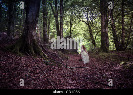 Woodland Fantasy Fotografie: ein Junge rote behaarte rothaarige Frau Mädchen trägt ein langes fließende Kleid hinunter eine Spur von einem verlassenen Haus selbst allein verloren in einem Wald Waldlichtung an einem Frühling Sommer Herbstnachmittag, UK Stockfoto