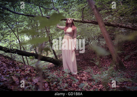 Woodland Fantasy Fotografie: ein Junge rote behaarte rothaarige Frau Mädchen trägt ein langes fließende Kleid zu Fuß durch sich allein in einen Wald Waldlichtung an einem Frühling Sommer Herbstnachmittag, UK Stockfoto