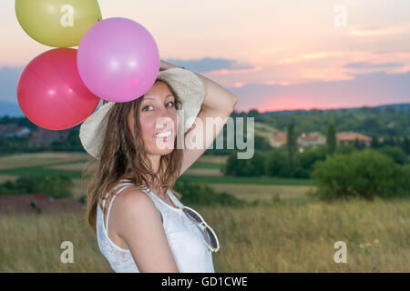 Junge Frau mit Ballons zum romantischen Sonnenuntergang Stockfoto